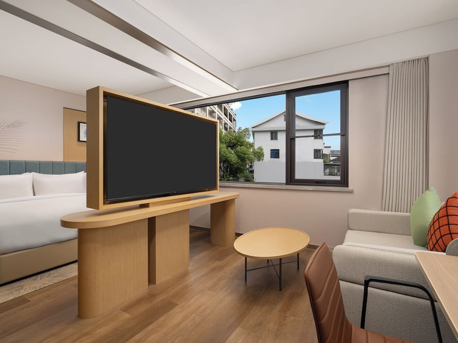 A modern hotel room with a bed, a desk with a flat-screen TV, a small round table, and a sofa.