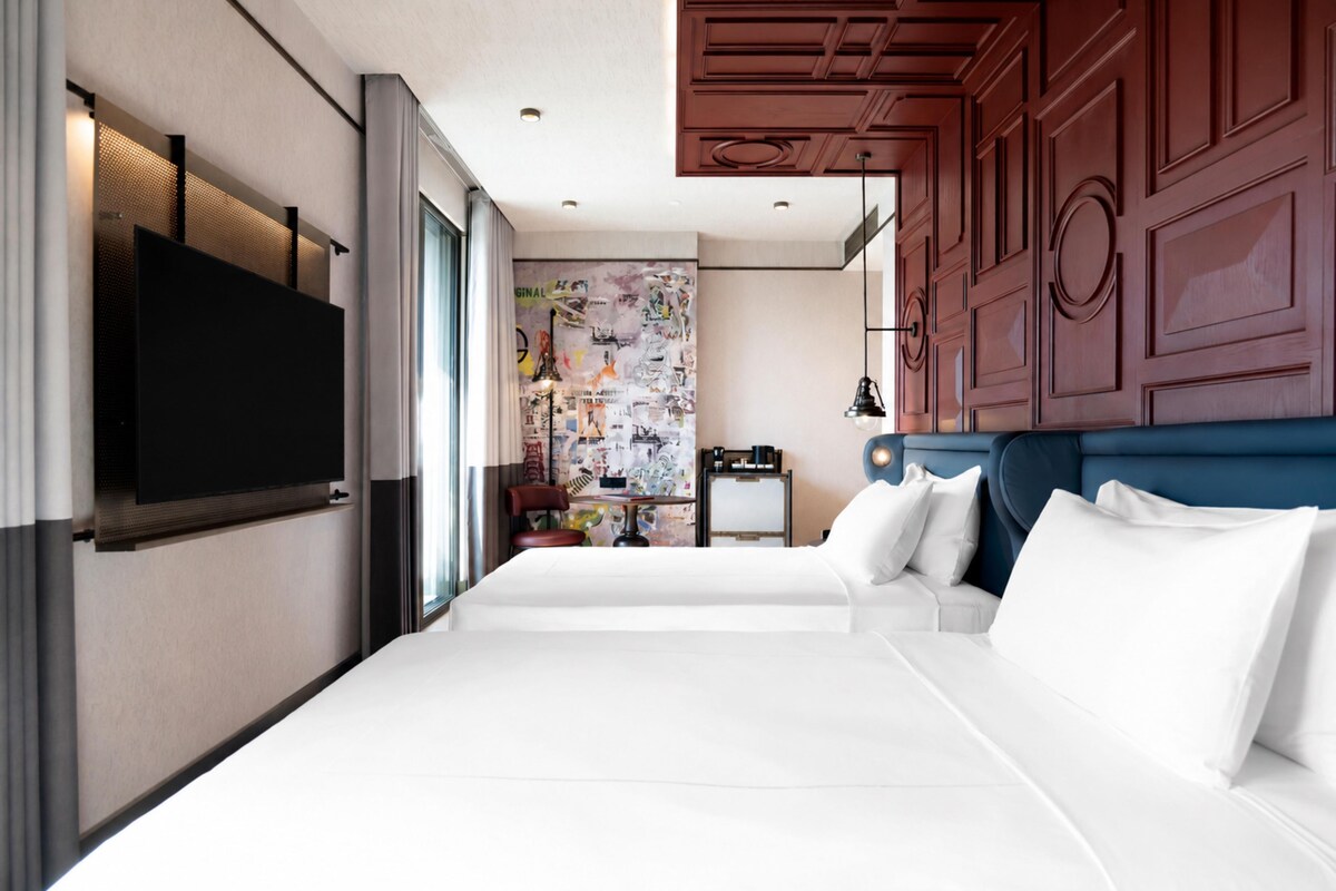 A hotel room with a large bed, a television mounted on the wall, and a decorative wall with various items.
