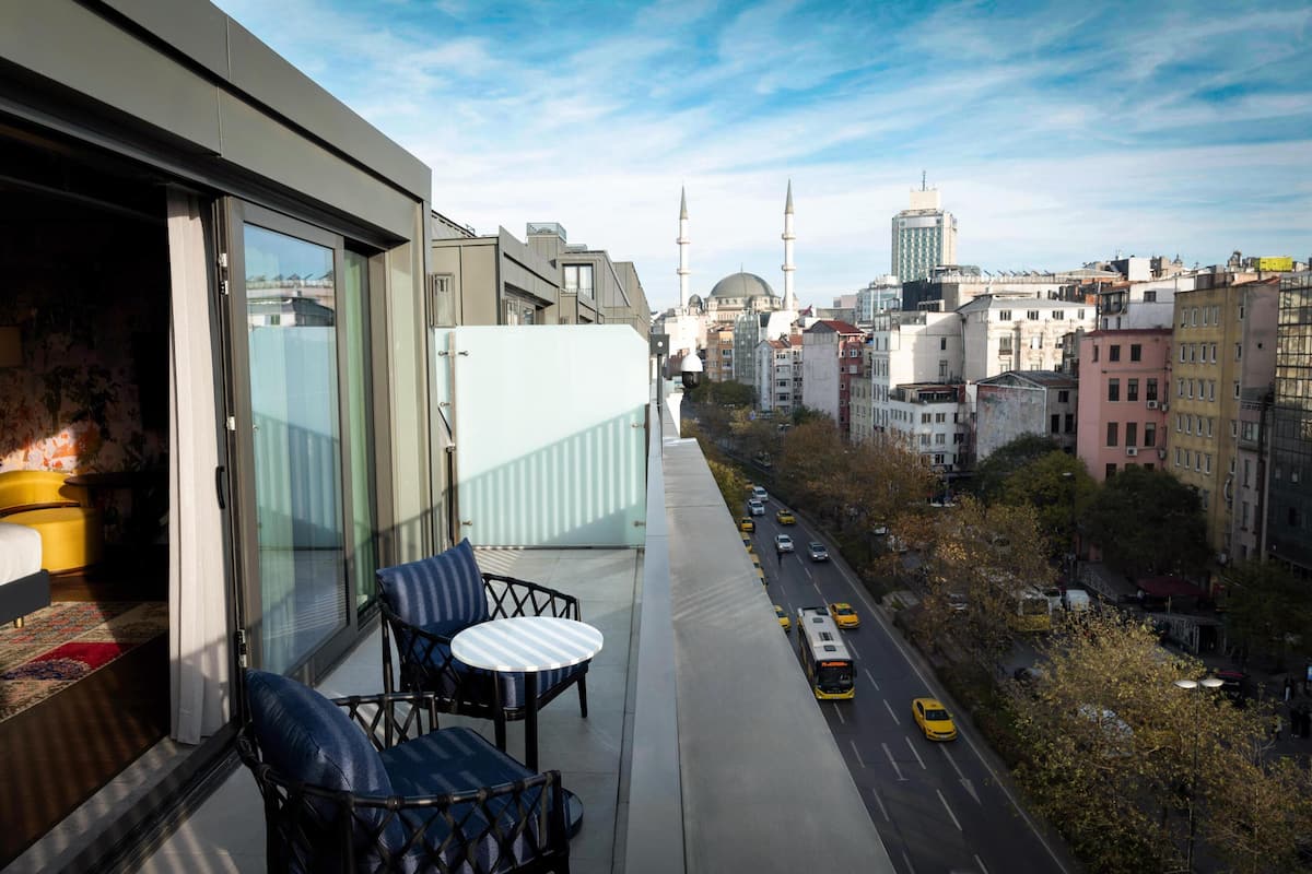 Un balcon offrant une vue sur le paysage urbain, avec notamment une mosquée dotée de minarets, un bâtiment moderne et une rue animée où circulent des véhicules.