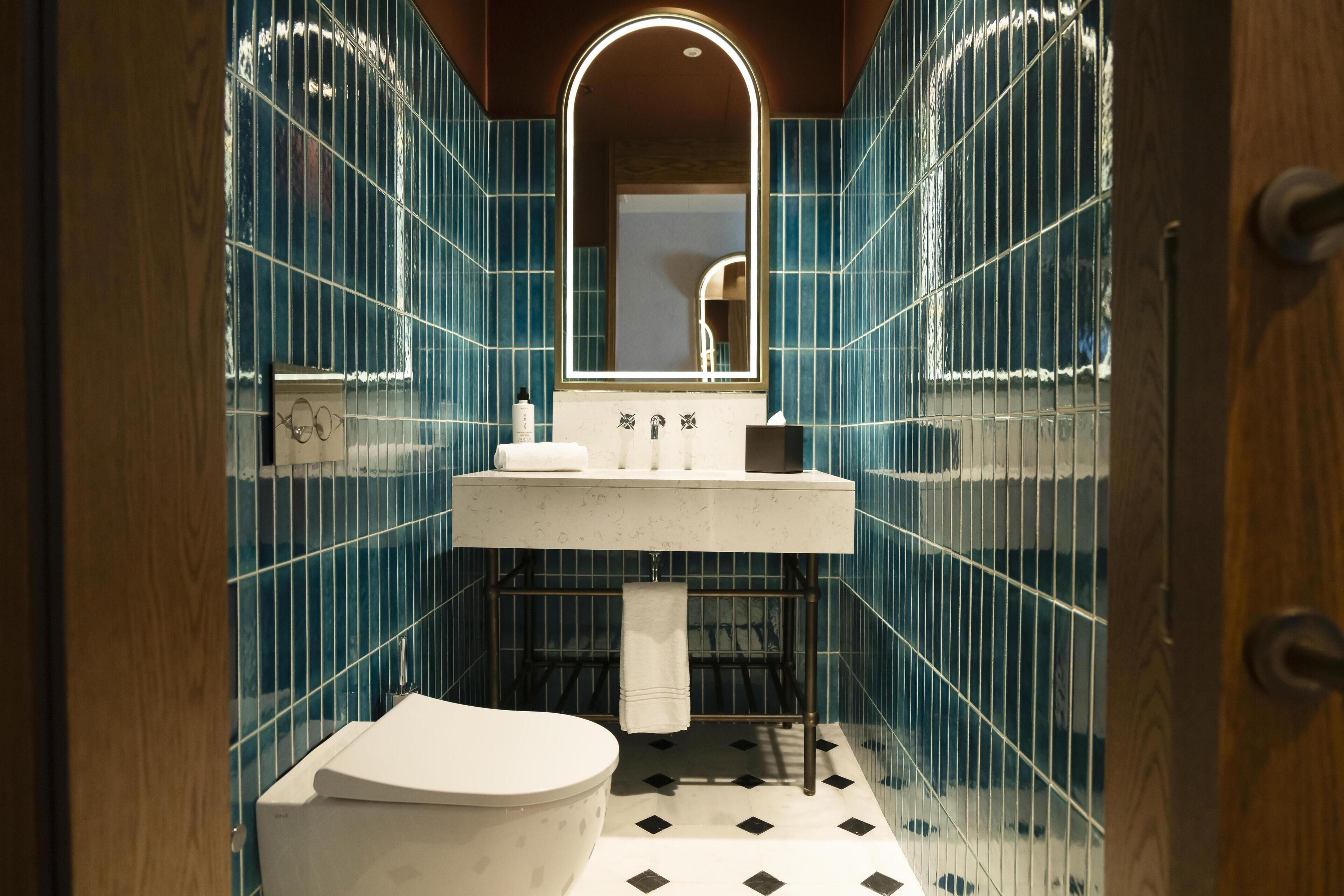 Ein Badezimmer mit Toilette, Waschbecken mit Spiegel und blauen Fliesen.