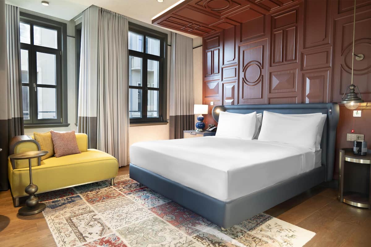 Une chambre d’hôtel avec un grand lit, un canapé jaune, un tapis à motifs et un lambris en bois.