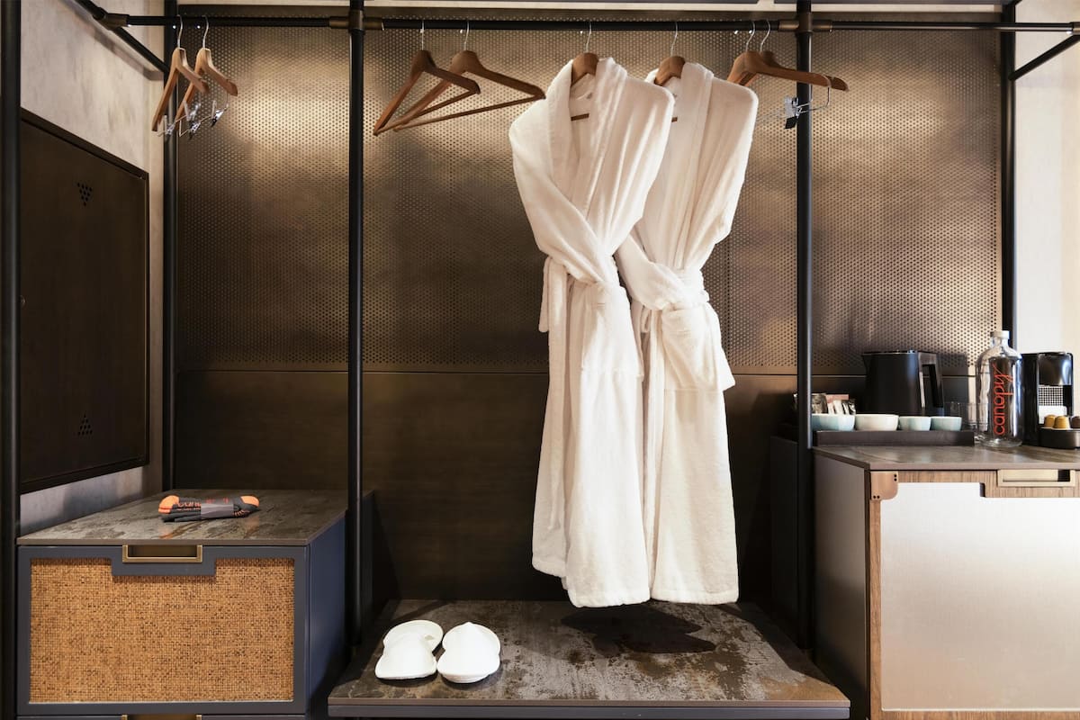 Une salle de bain avec un porte-serviettes sur lequel sont pliés deux peignoirs blancs, une paire de chaussons posée sur le sol et une petite étagère contenant des articles de toilette.