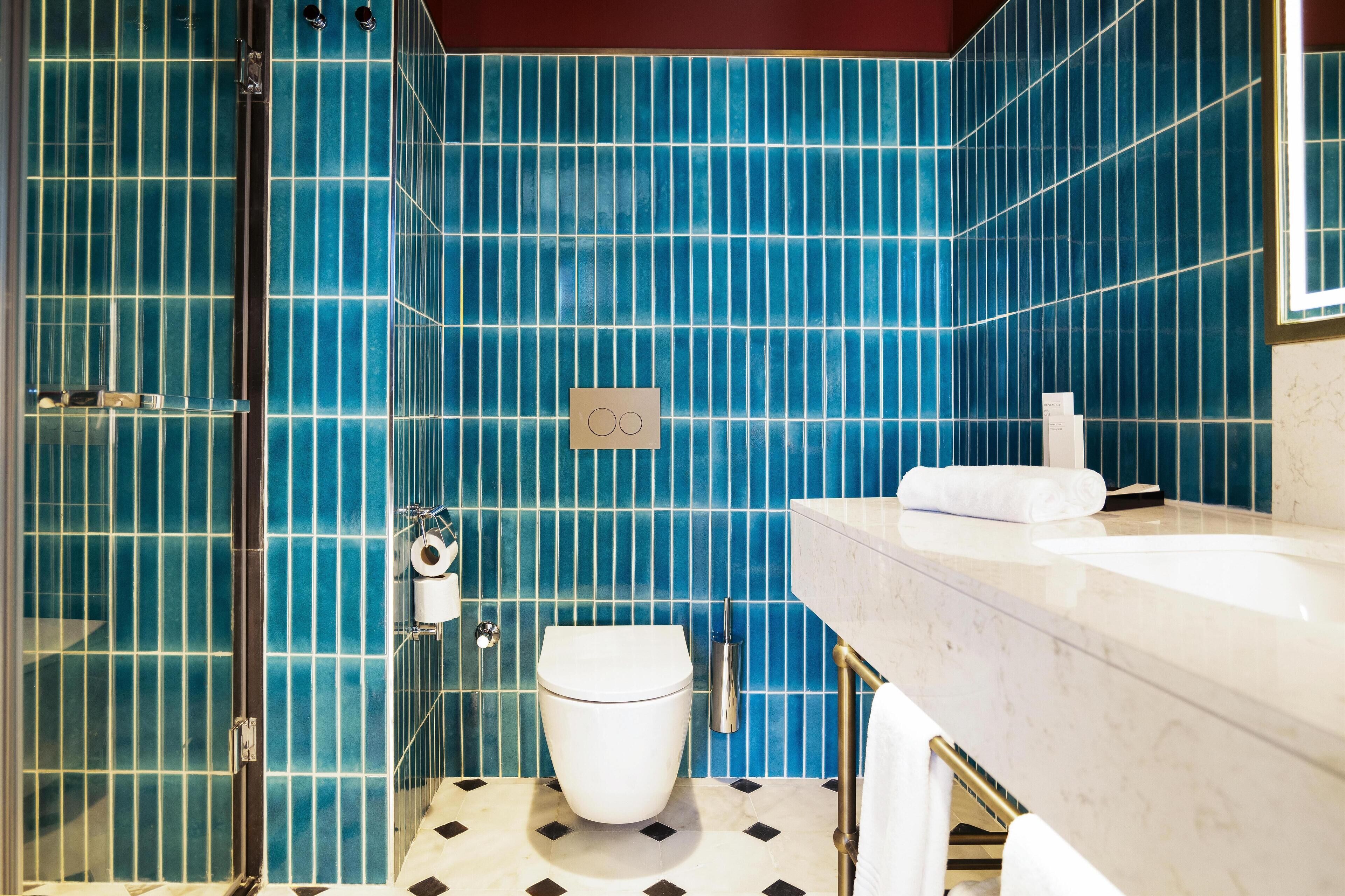 A bathroom with blue-tiled walls, a white toilet, a marble sink, and a glass shower enclosure.