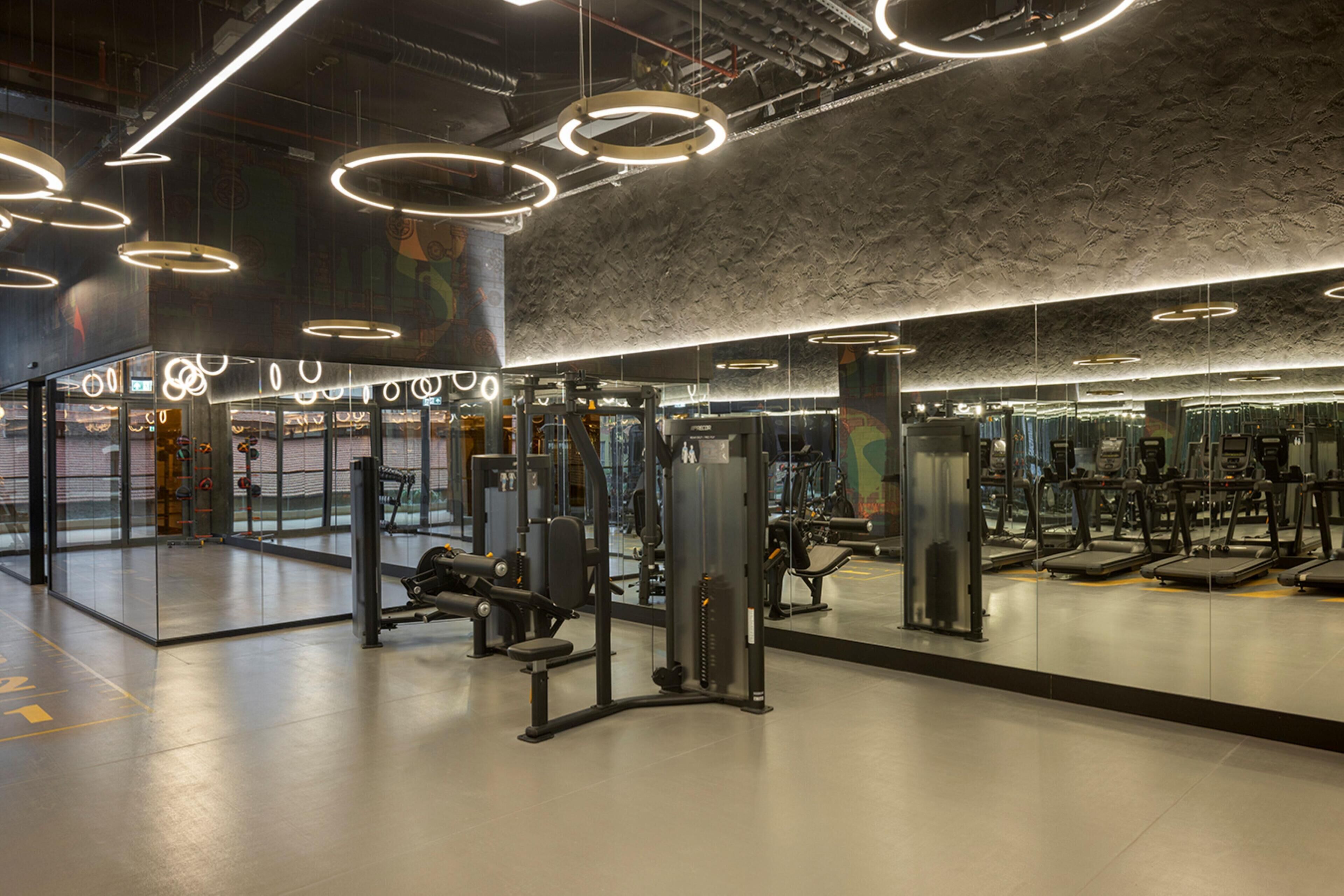 A modern gym with various exercise equipment, large mirrors, and circular ceiling lights.