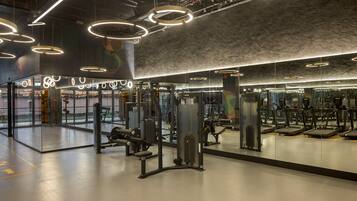 A modern gym with various exercise equipment, large mirrors, and circular ceiling lights.