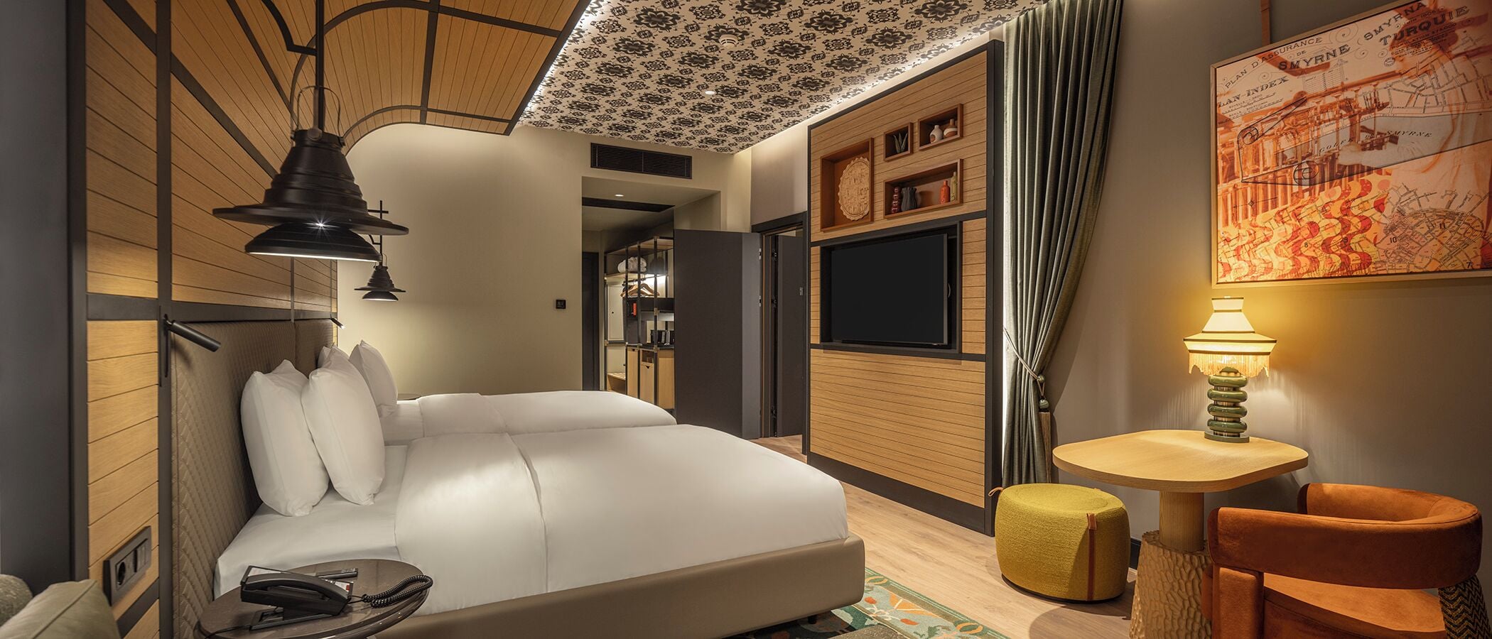 A modern hotel room with a bed, bedside table, lamp, and a small seating area with a chair and ottoman.