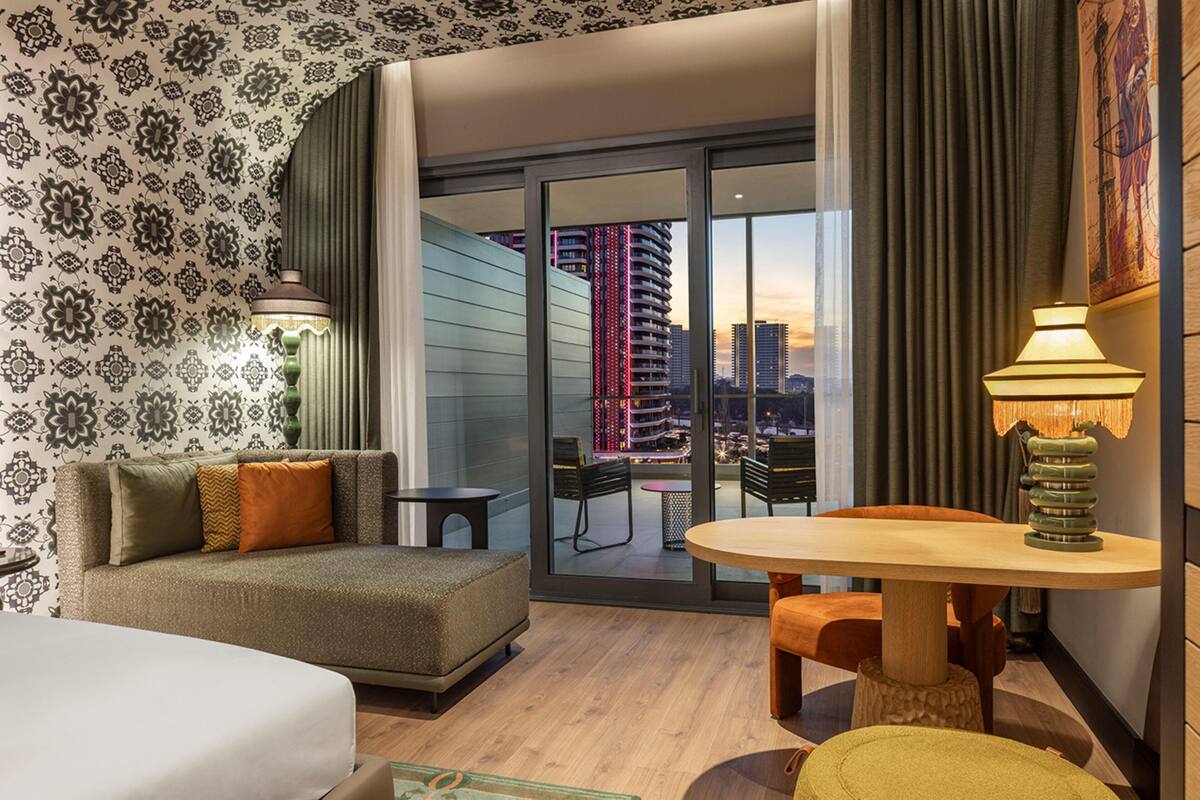 Une chambre d’hôtel avec un canapé, une table ronde et une vue sur le paysage urbain au coucher du soleil.
