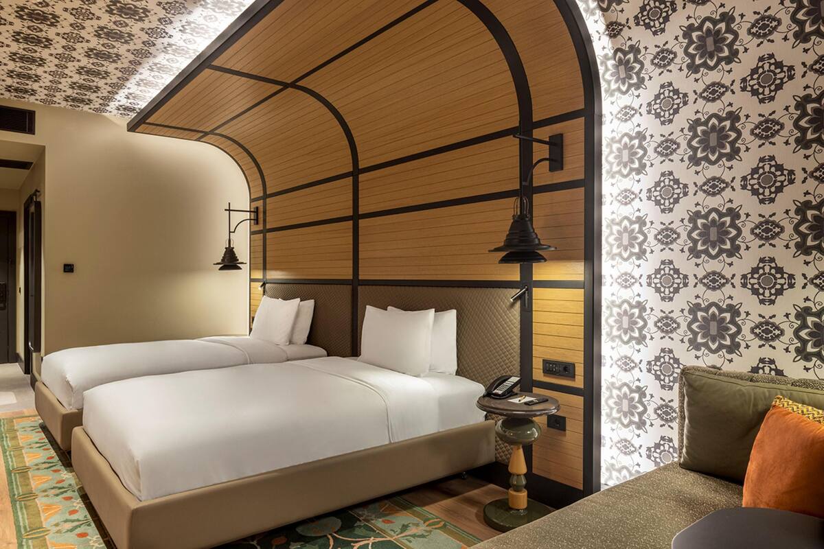 Une chambre d’hôtel avec deux lits, un plafond en bois, un papier peint à motifs et une petite table avec un téléphone.