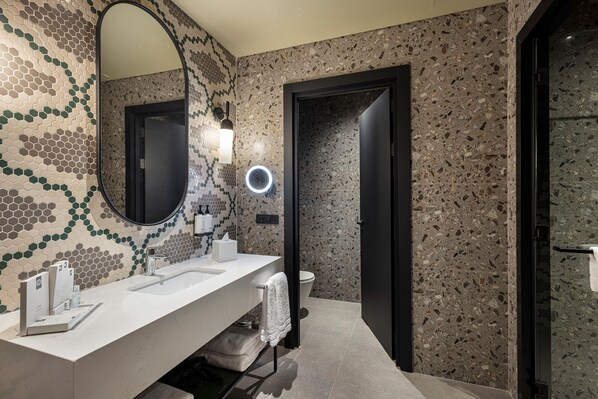 Un baño moderno con un lavamanos blanco, un espejo redondo y un inodoro.