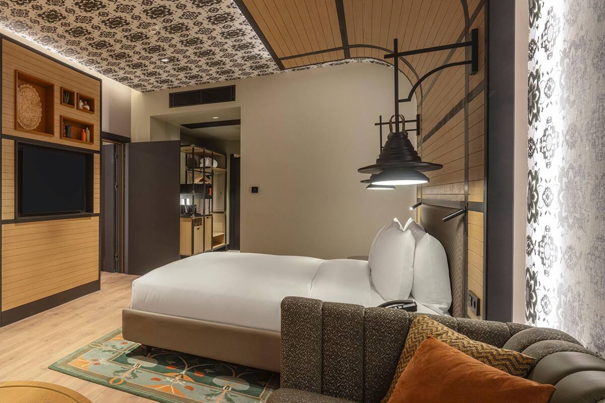Une chambre d’hôtel moderne, équipée d’un lit, d’une petite table avec une lampe, d’une chaise et d’un élément décoratif mural.