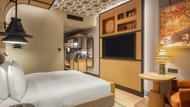 Ein modernes Hotelzimmer mit einem Bett, einem kleinen Tisch, einem Sessel und einem an der Wand befestigten Fernseher.