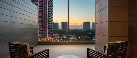 Un balcón con dos sillas y una mesa pequeña, con vistas a un paisaje urbano de edificios altos y un atardecer.