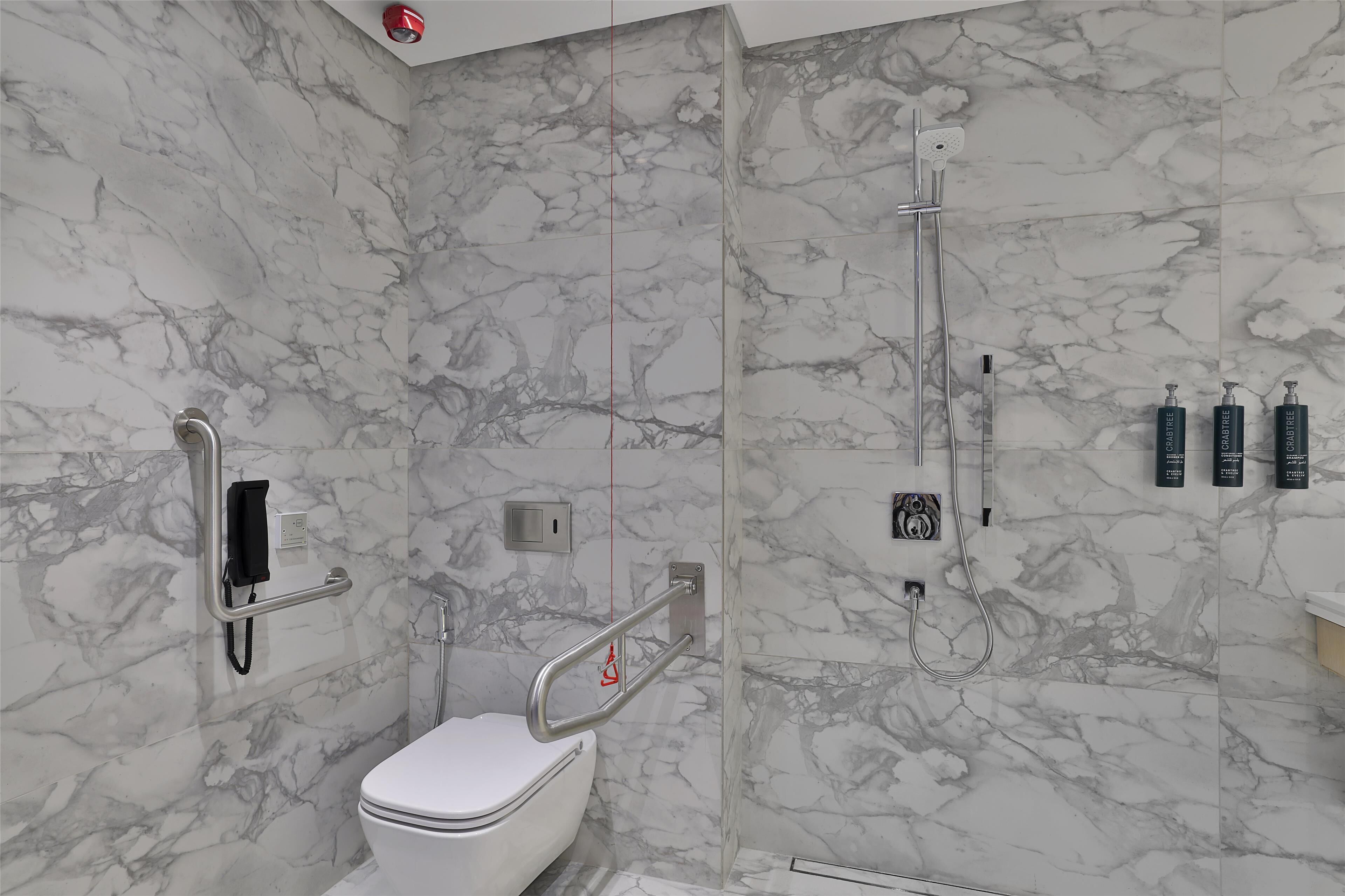 A bathroom with a marble wall, a toilet, a shower, and a handrail.