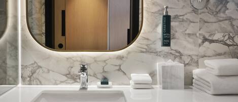 A bathroom with a marble sink, a mirror, a hand soap dispenser, and neatly stacked towels.