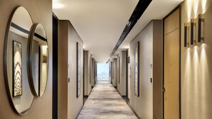 Un largo y estrecho pasillo de hotel con paredes espejadas, puertas y cuadros enmarcados.