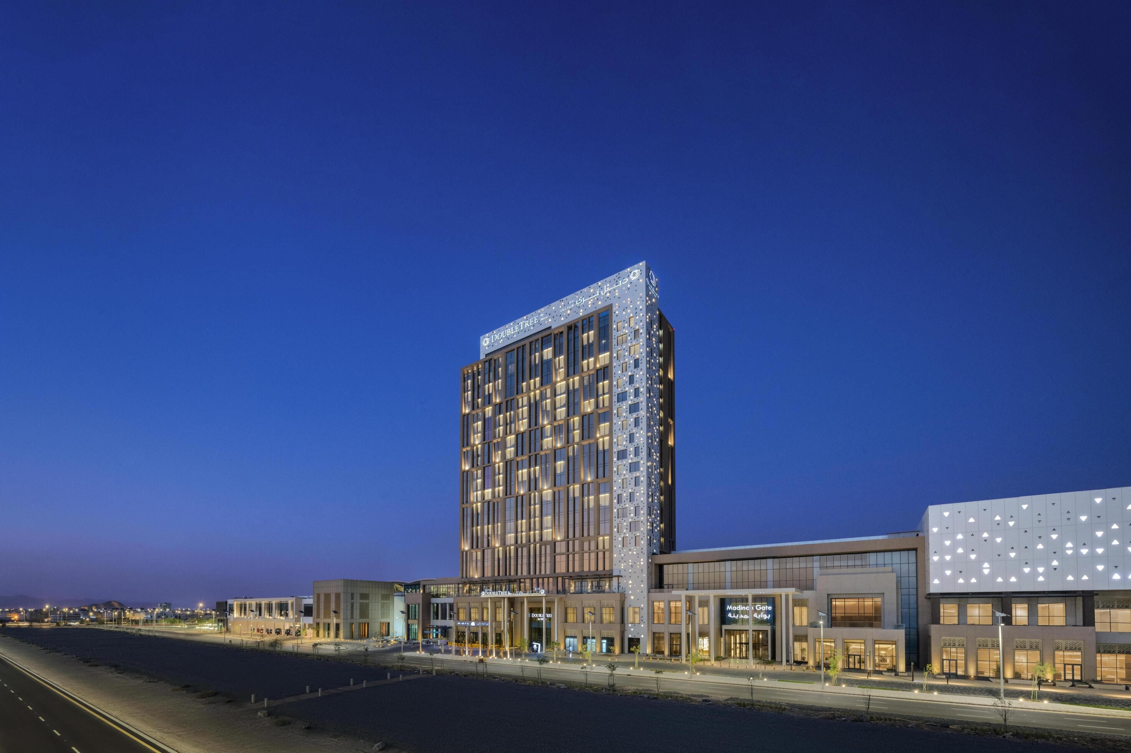Een modern hotel met een opvallend rechthoekig gebouw, diverse winkels op begane grond en uitzicht op het strand.