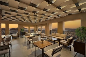 Un salón moderno con techo geométrico, asientos cómodos y ventanas amplias con vistas a la ciudad.