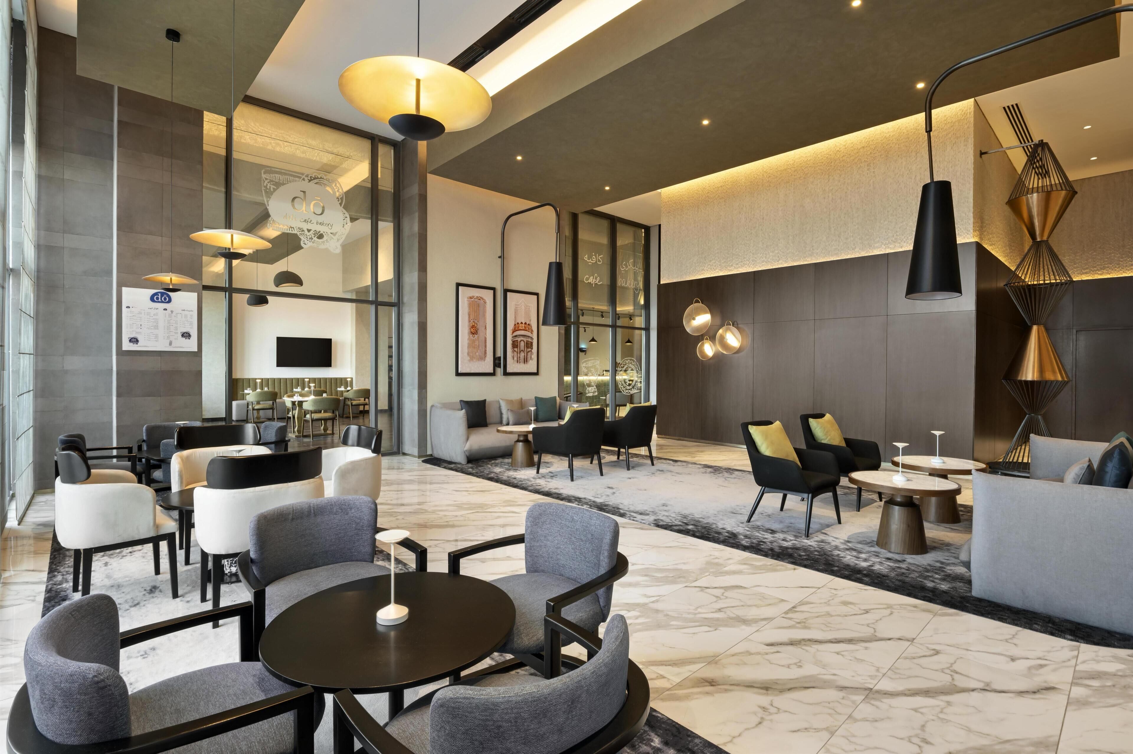 A modern hotel lobby with seating areas, a coffee bar, and a television screen.