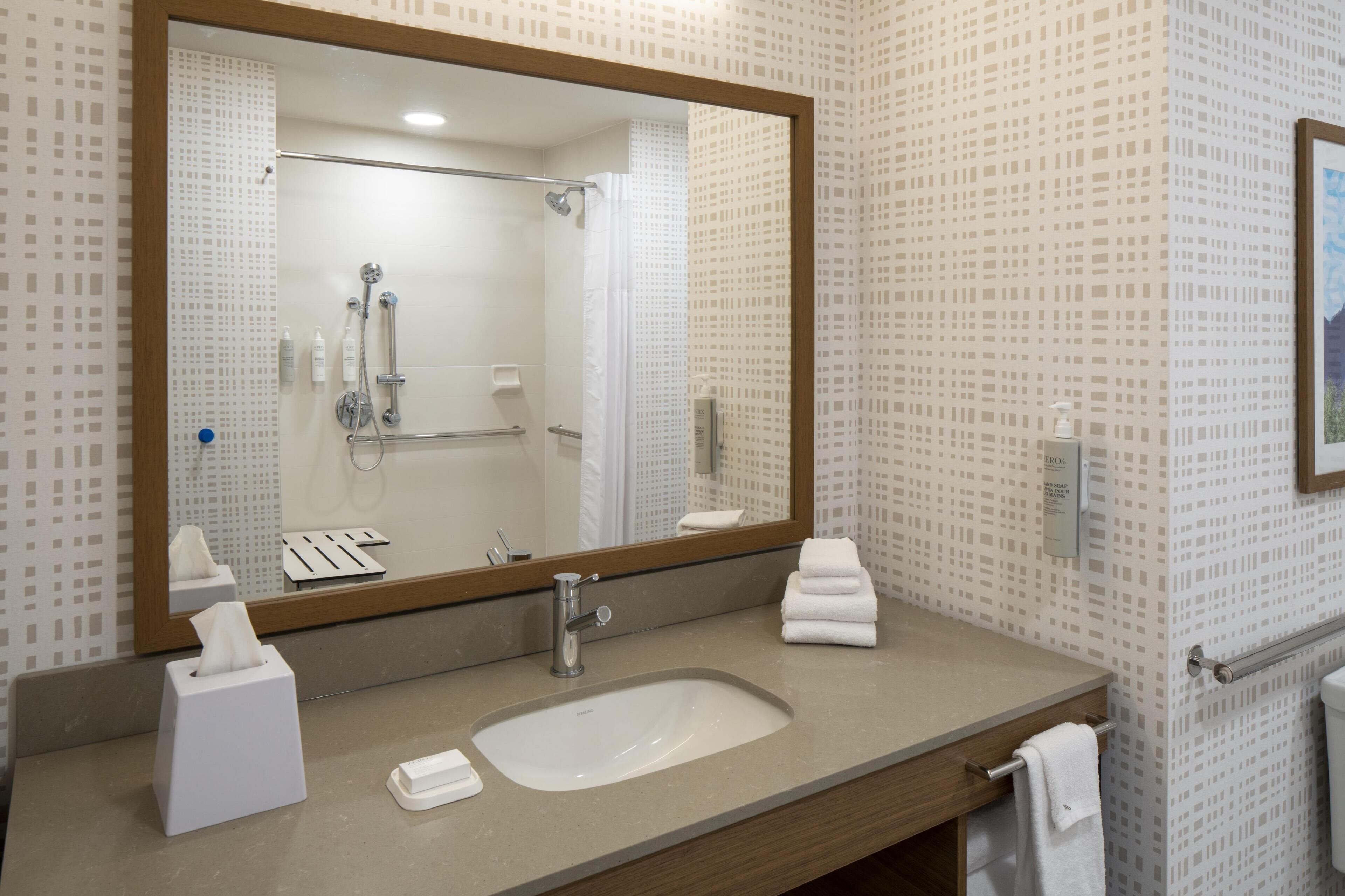 A bathroom with a large mirror, a sink, a shower, and a towel rack.