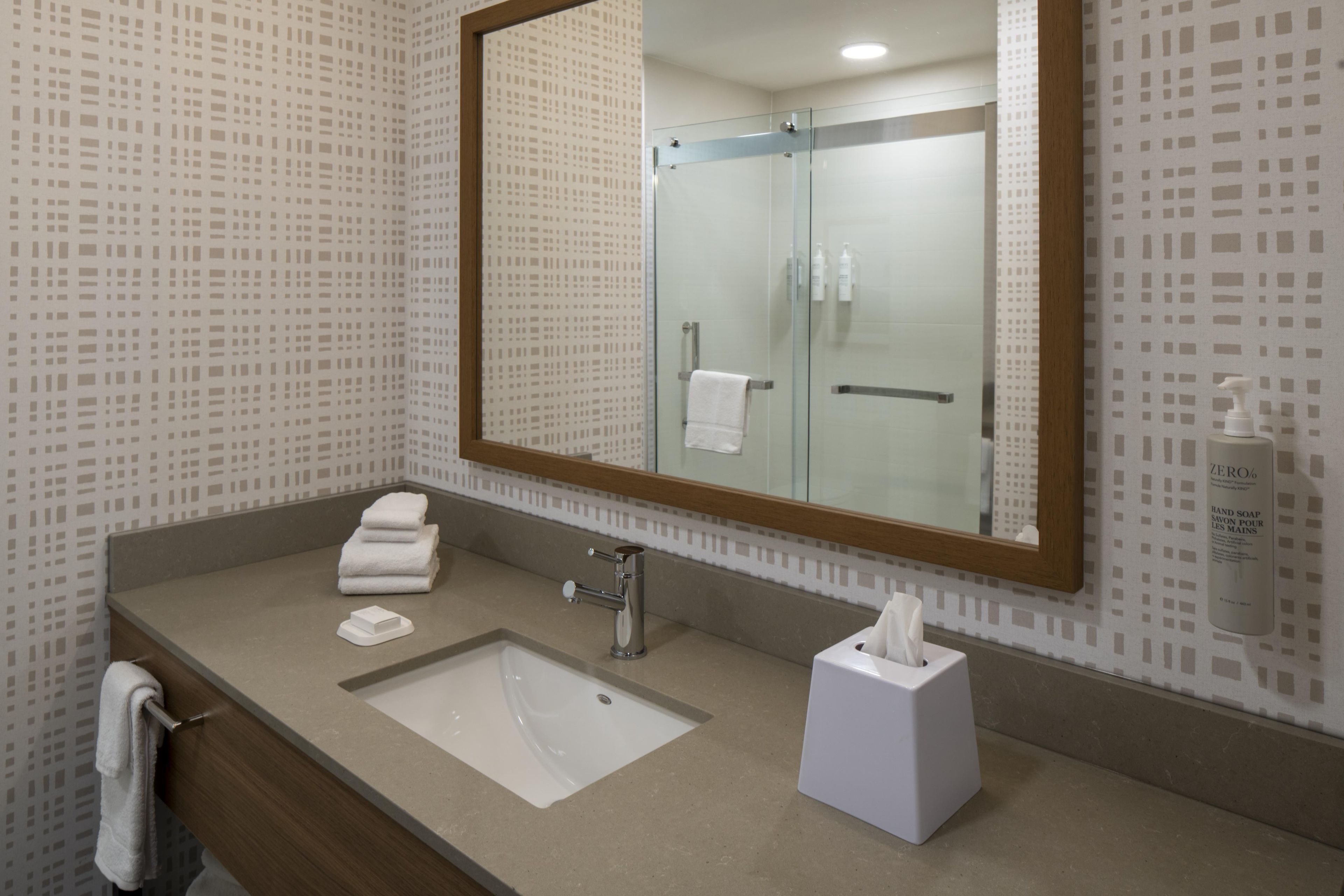A bathroom with a large mirror, a sink, a towel rack, and a hand soap dispenser.