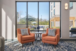 Habitación de hotel con dos sillones naranjas, un tapete estampado y vistas al área de estar exterior a través de ventanas amplias.