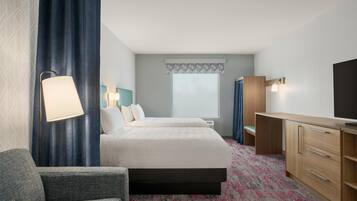 A hotel room with a bed, a desk, a chair, a TV, and a window.