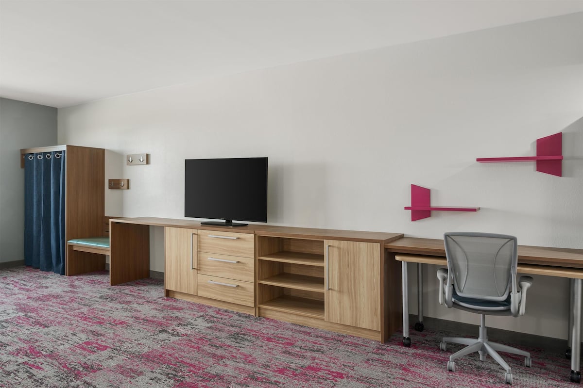 A room with a wooden desk, a television, a chair, and a blue curtain.