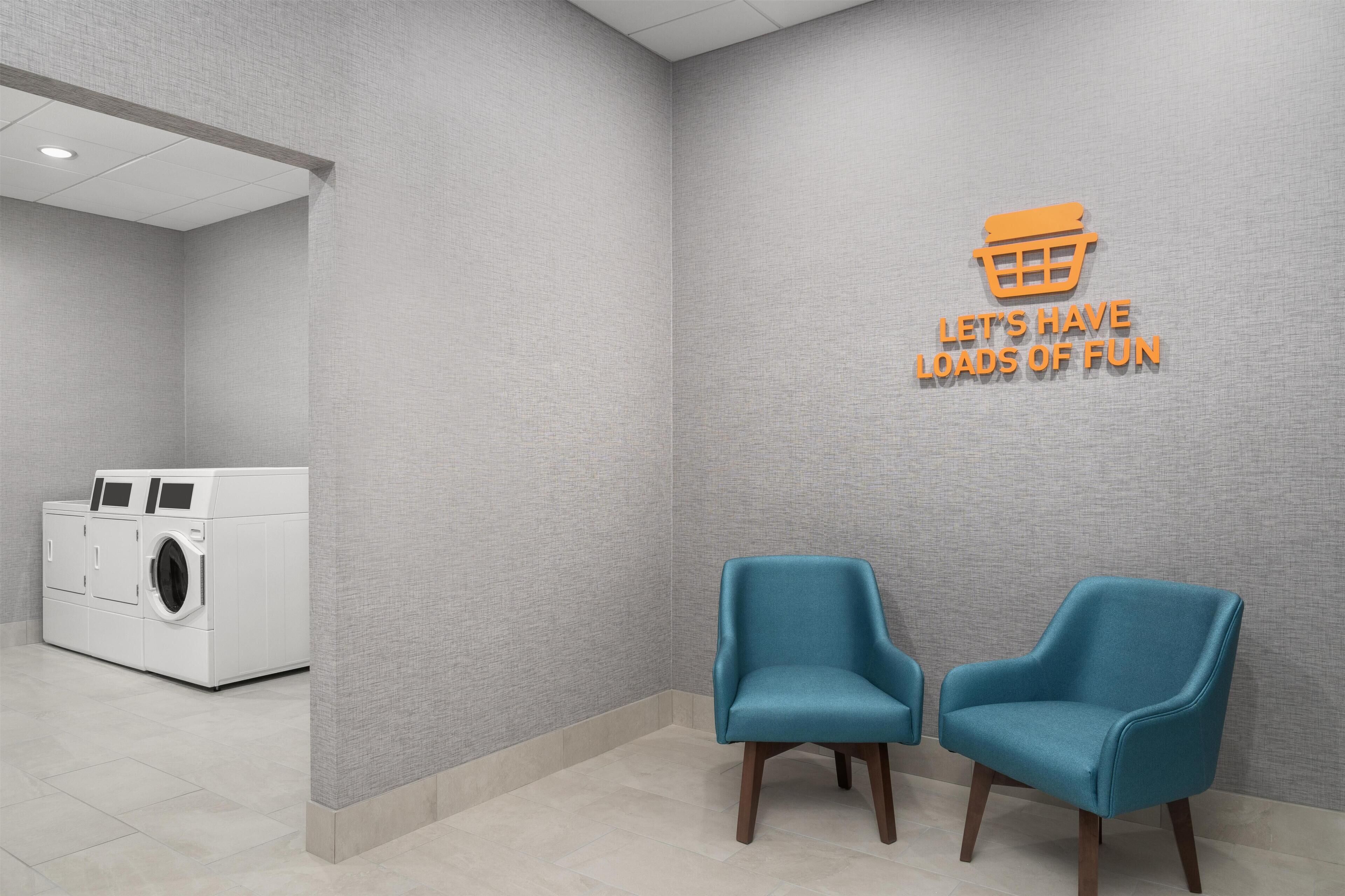A laundry area with a washing machine, two blue chairs, and a wall with a text sign.
