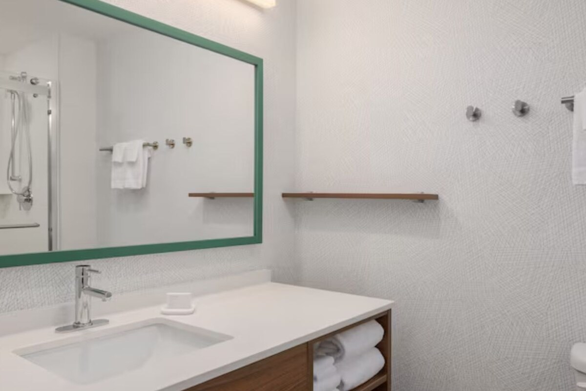 Un baño con un espejo grande, lavabo, ducha y toallero.