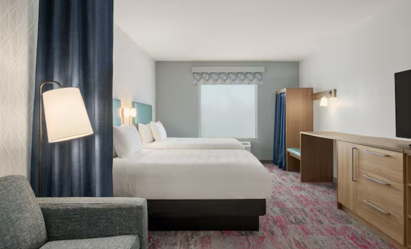Una habitación de hotel con una cama, un escritorio, una silla, una lámpara y un televisor.