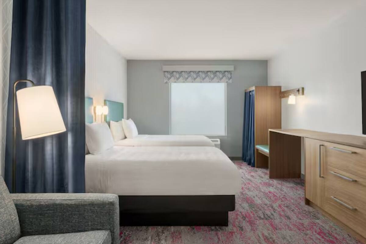 A hotel room with a bed, a desk, a chair, a lamp, and a television.