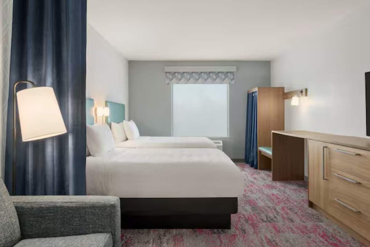 Una habitación de hotel con una cama, un escritorio, una silla, una lámpara y un televisor.