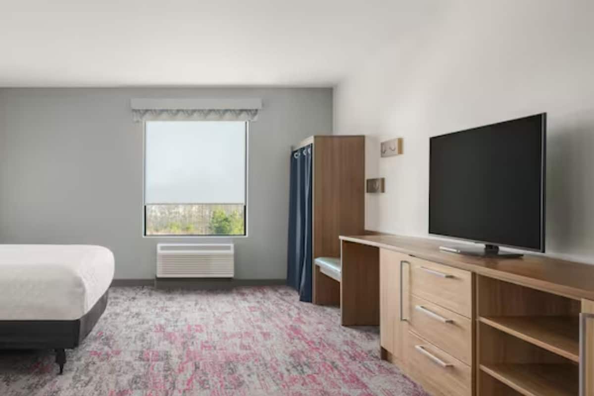 A hotel room with a bed, a TV, a desk, and a window.
