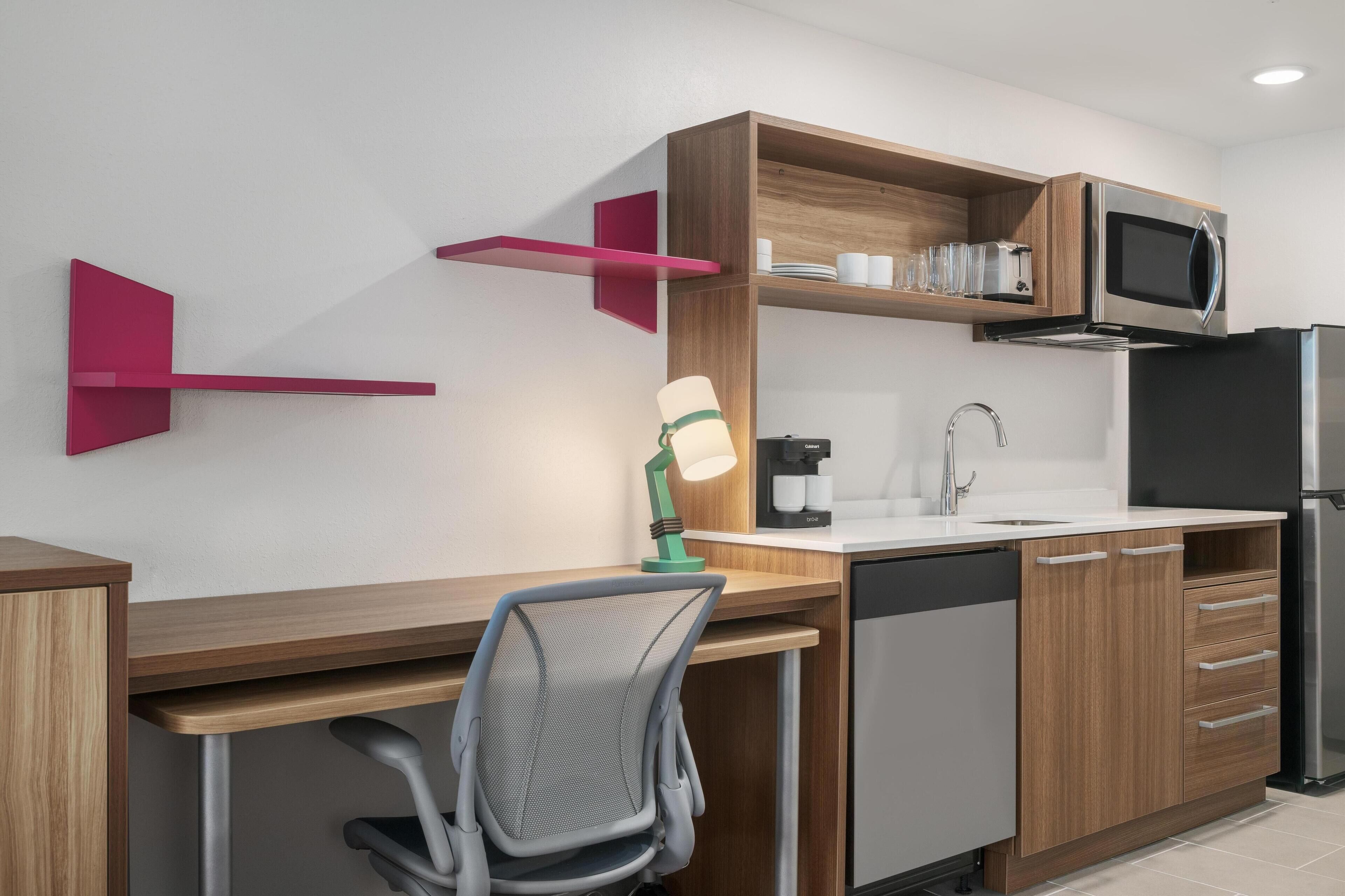 A modern kitchen with wooden cabinets, a built-in microwave, a sink, and a chair.