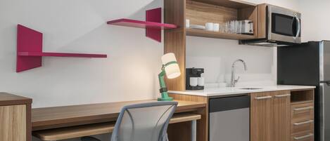 A modern kitchen with wooden cabinets, a built-in microwave, a sink, and a chair.