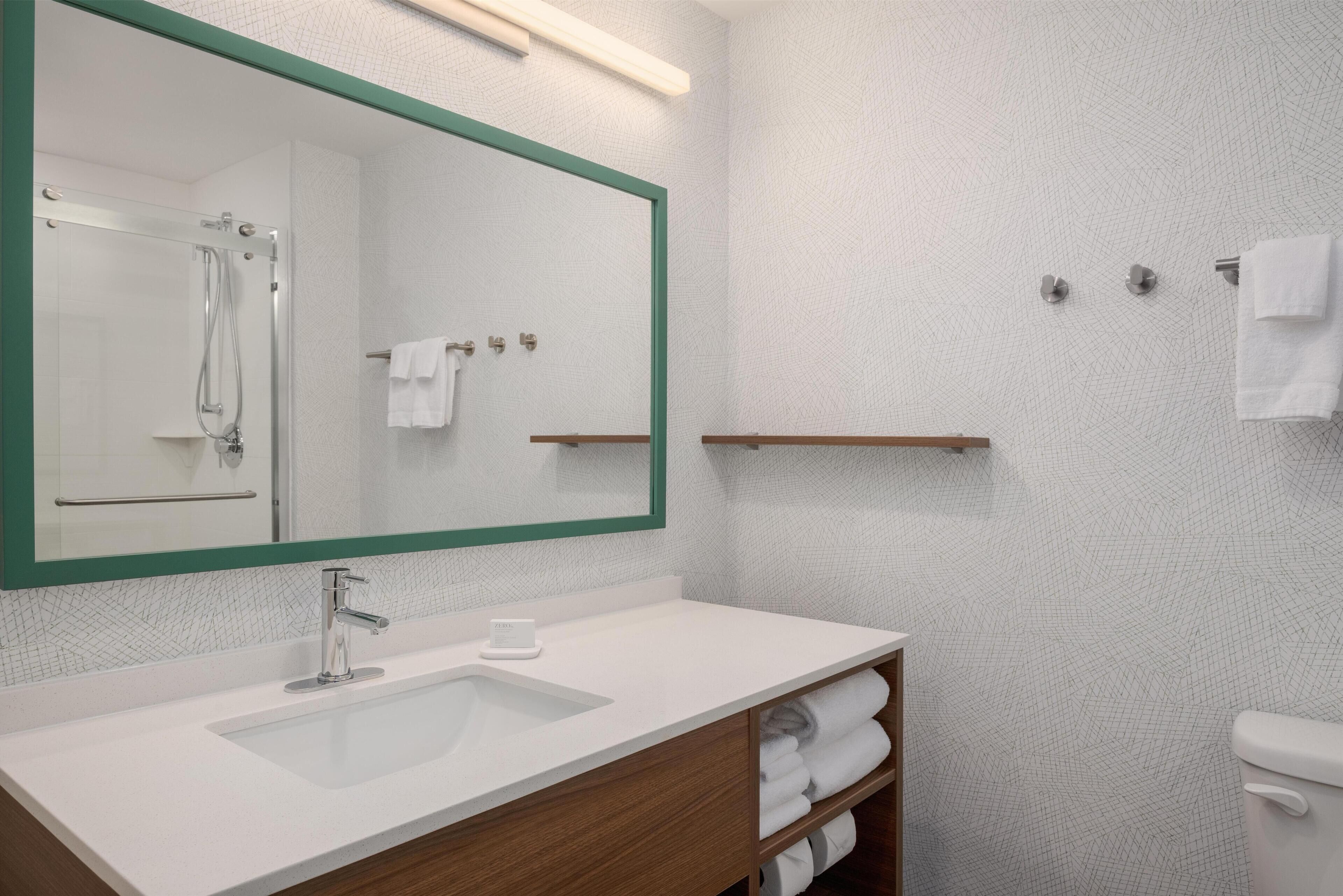 A bathroom with a large mirror, a sink, a shower, and a toilet.