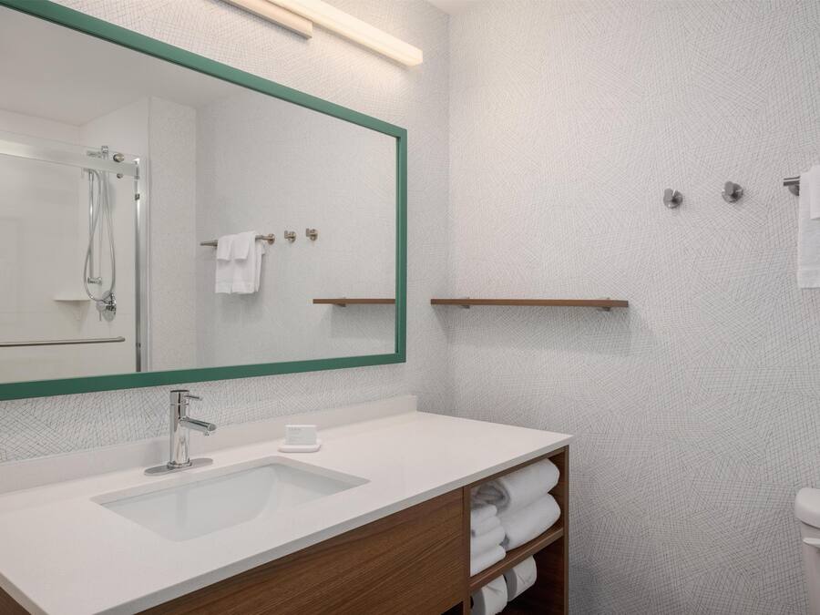A bathroom with a large mirror, a sink, a shower, and a toilet.
