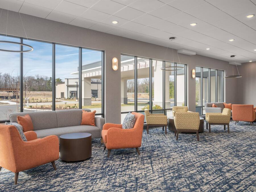A hotel lobby with a large seating area, a reception desk, and a view of the outside.