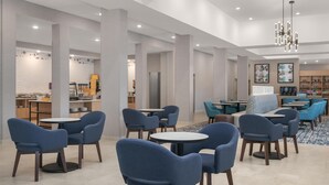 Rebedor d'hotel modern amb taules rodones i cadires blaves, una barra de cafè i una zona de seients amb sofàs blaus.