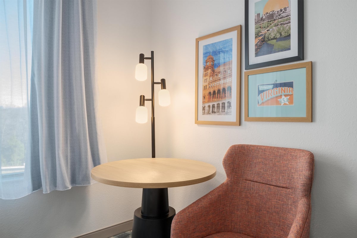A room with a round table, a chair, a floor lamp, and two framed pictures on the wall.
