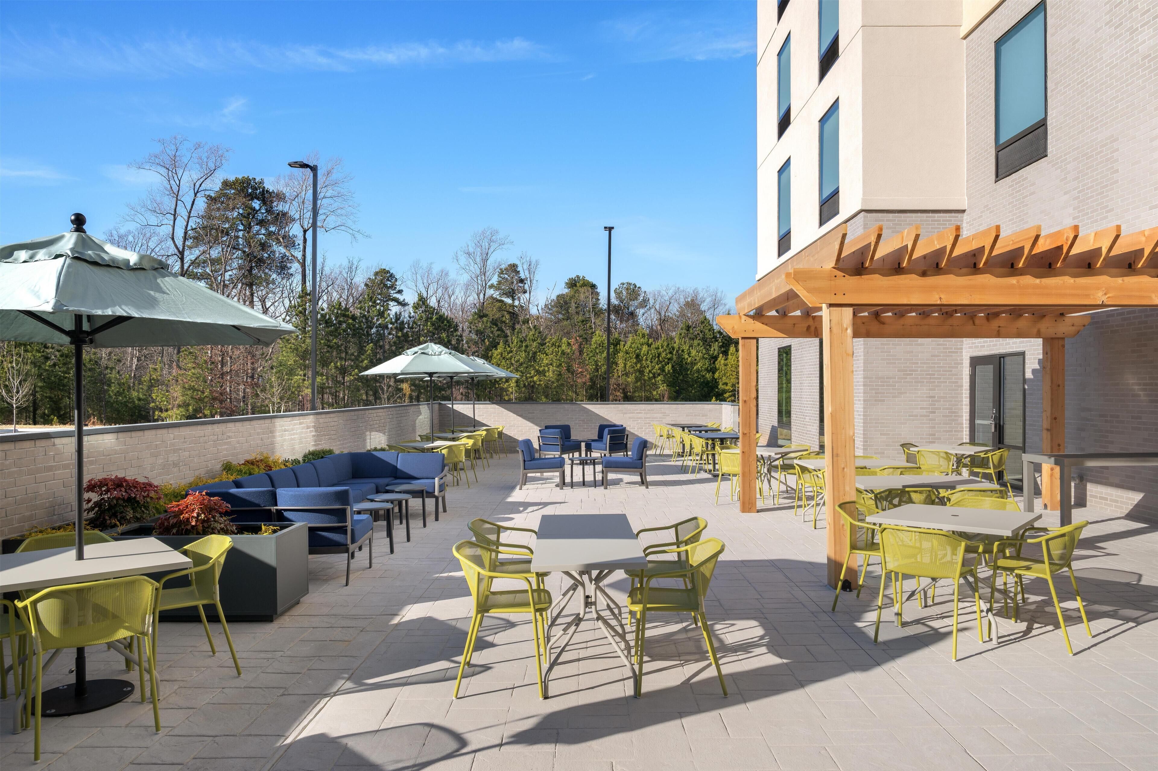 An outdoor patio with tables and chairs, a pergola, and a building in the background.