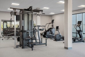 Un gimnasio con diversos equipos de ejercicio, entre ellos una máquina de pesas, cintas de correr y mancuernas.