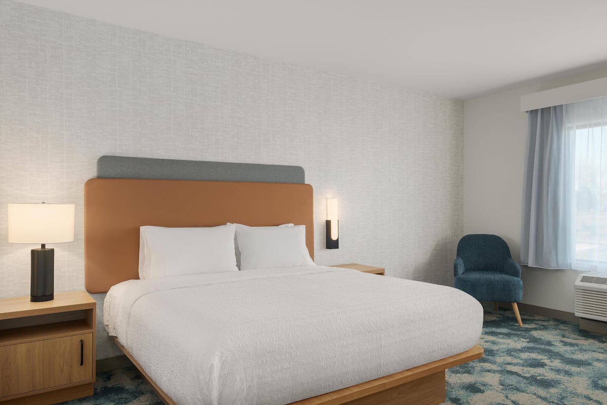 A hotel room with a bed, a nightstand, a chair, a lamp, and a window with curtains.