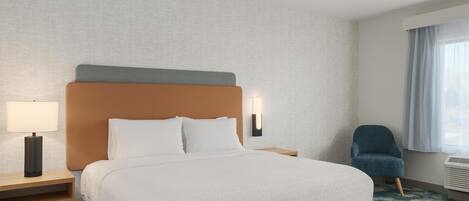 A hotel room with a bed, a nightstand, a chair, a lamp, and a window with curtains.
