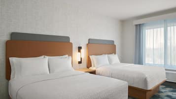 A hotel room with two beds, a nightstand with a lamp, a large window with curtains, and a textured wall.
