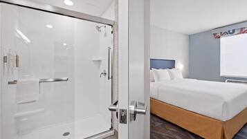 Een hotelkamer met een glazen douchecabine, een bed met hoofdeinde en een wandgemonteerde airconditioning.