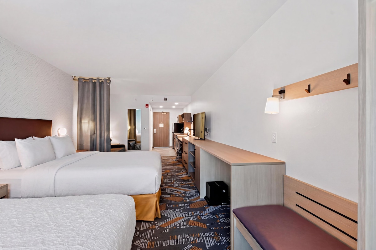 A hotel room with a large bed, a desk, a chair, a television, and a bathroom visible through an open door.