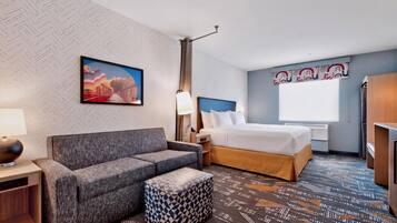 Een hotelkamer met een bank, een bed, een nachtkastje, een lamp en een kamerbreed tapijt met een patroon.