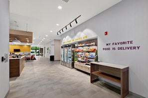 A modern food delivery service area with a refrigerated display and a counter. - Home2 Suites By Hilton Raleigh Crabtree (Raleigh)
