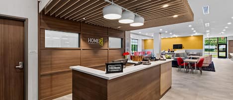Un hall d'accueil d'hôtel avec un comptoir de réception en bois, un panneau indiquant « Hilton Honors », et un aménagement intérieur moderne.